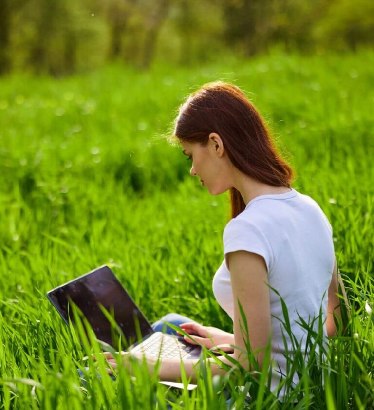 Dans une grande prairie ensoleillée avec des herbes hautes, une art-thérapeute se tient devant son ordinateur et participe aux ateliers en ligne.