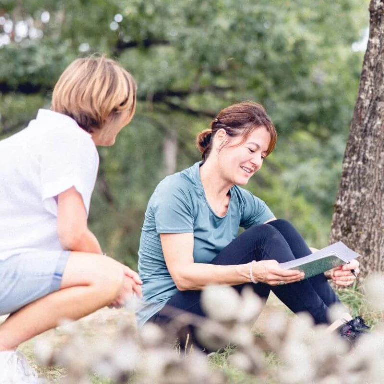 En plein cœur du Jura, une participante coach relit ses notes prises sur son carnet et partage ses observations à la formatrice en écothérapie.