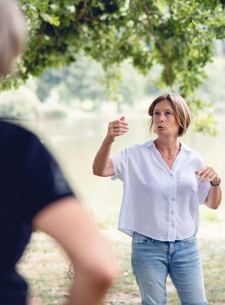 Zoom sur Ilse Geusens en train d’enseigner dans la nature, avec les bras en mouvement.