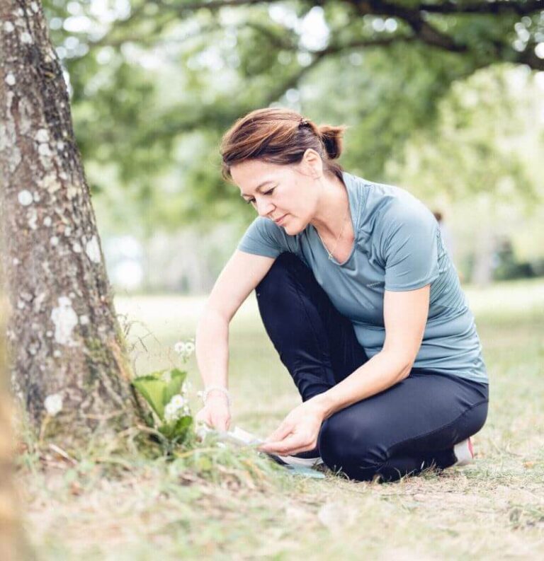 Dans une forêt, une naturopathe proche d’un tronc arbre relit attentivement les exercices à réaliser.