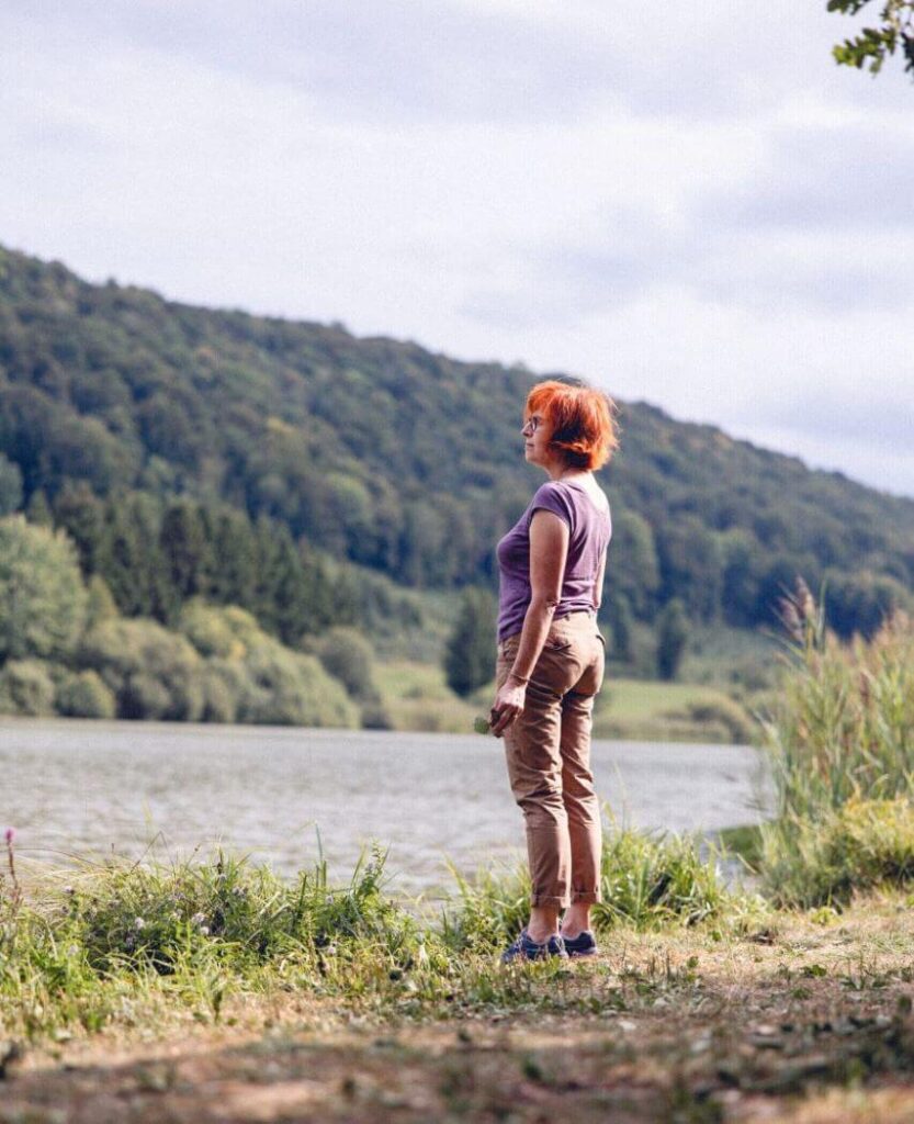 Debout, une patiente observe avec attention un très beau paysage composé d’un lac et de montagnes.