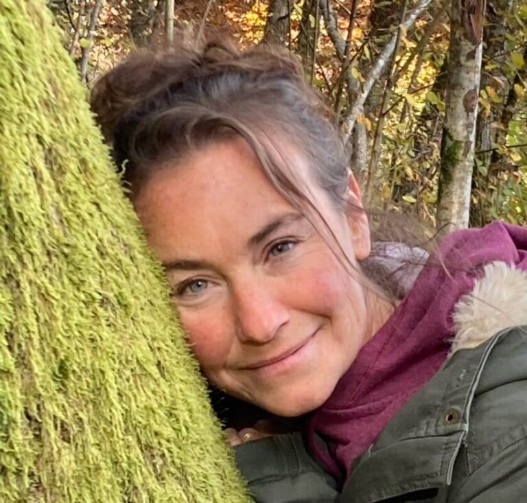 Photo portrait de Charlotte Schwartz, avec la tête posée contre un arbre.