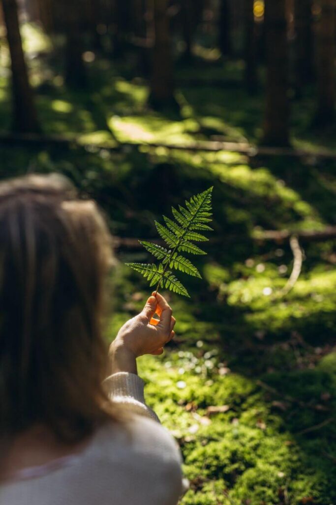 Dans les bois, une psychiatre observe avec attention une feuille de fougère qu’elle tient dans sa main droite.