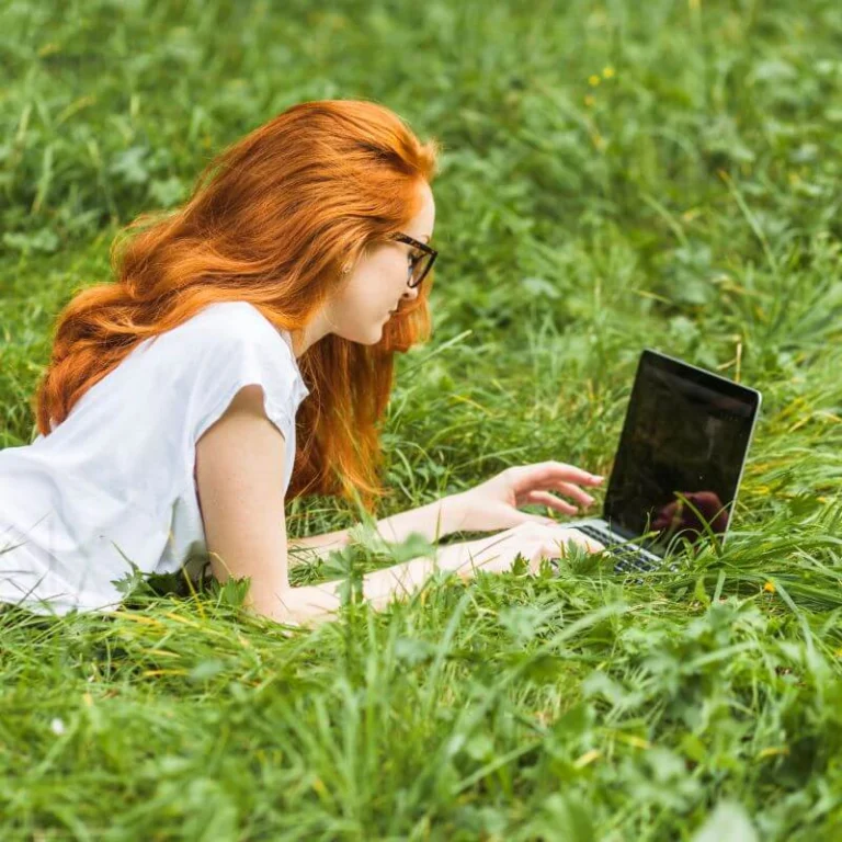 Une psychiatre est devant son ordinateur, assise dans l’herbe et participe à un atelier en ligne d’écopsychologie.