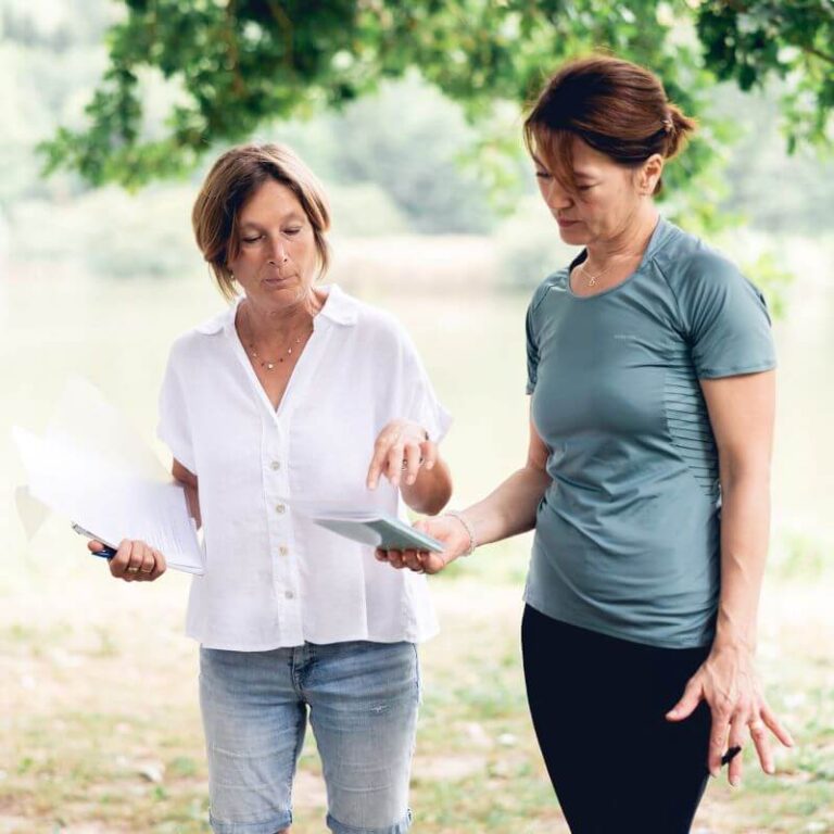 Sous un très bel arbre, une psychothérapeute montre ses notes écrites à la formatrice en écothérapie, qui lui apporte enseignements et éclairages personnalisés.