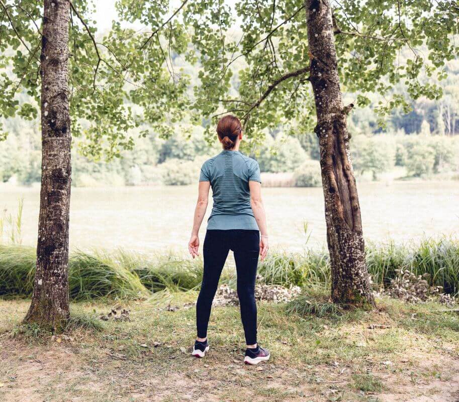 Devant un lac et dos à la caméra, une sophrologue prend le temps de ressentir son corps en faisant quelques mouvements.