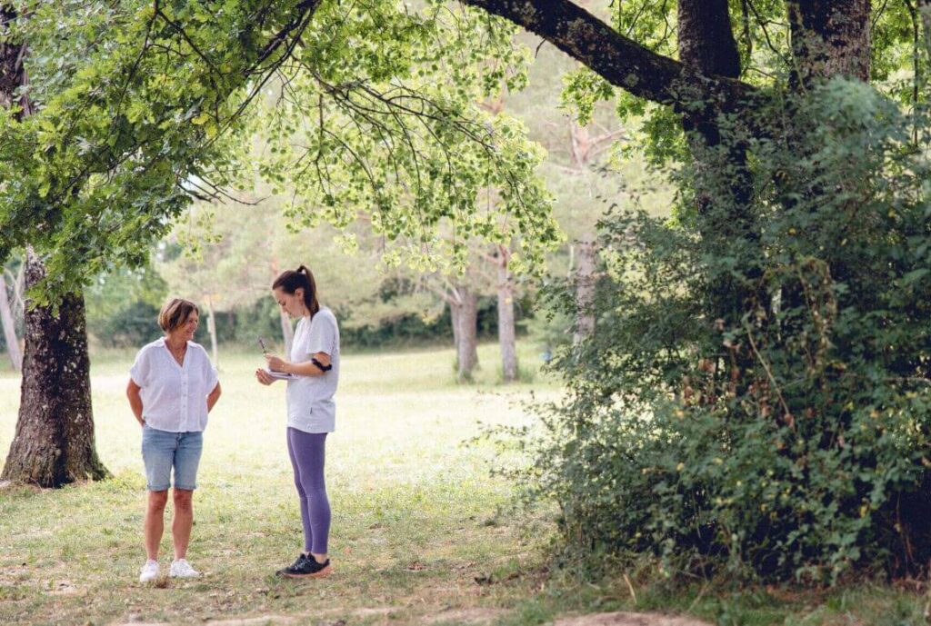 Dans une magnifique forêt et aux côtés de sa thérapeute, la cliente est inspirée au contact de la nature et note ses idées dans un cahier.